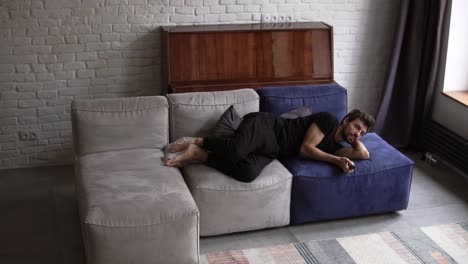 Happy man falling on the sofa, switch on the tv at home in the living room