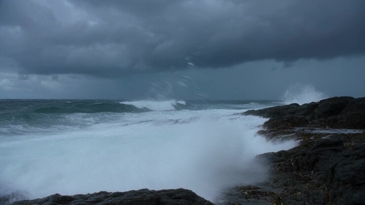 Le ressac s'écrasant sur un promontoire rocheux projette de hautes gerbes d'eau sur une plateforme rocheuse, tandis que les houles de tempête s'intensifient.