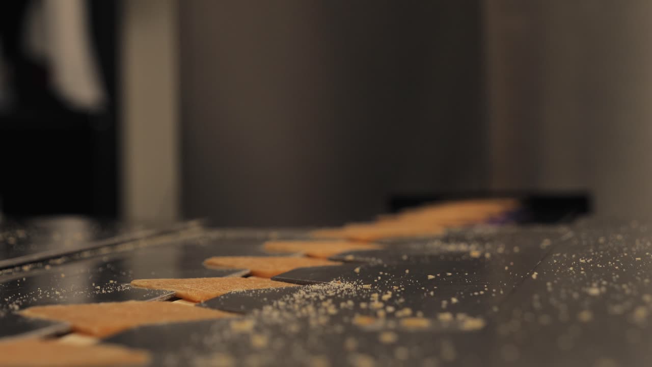 Primo piano statico di caramelle di zucchero quadrate su una superficie di una macchina in acciaio inossidabile, mentre una mano entra nell'inquadratura per posizionare le caramelle nella linea di produzione di dolciumi