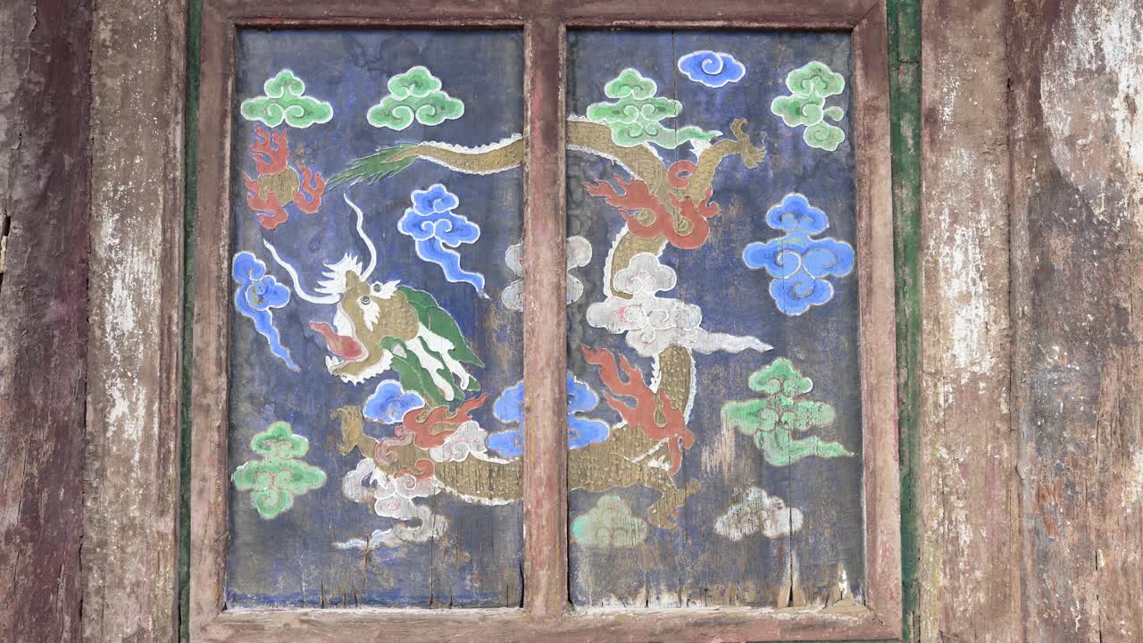 Ancient painted dragon on a wooden window shutter at Erdene Zuu Monastery, Mongolia. The traditional Buddhist art features a mythical creature and clouds on a weathered blue panel