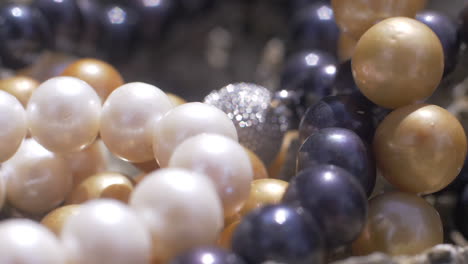 Close-up-cinematic-shot-of-various-pearl-necklaces-in-white,-blue-and-yellow-with-silver-jewellery-on-rock,-120-FPS,-Slomo