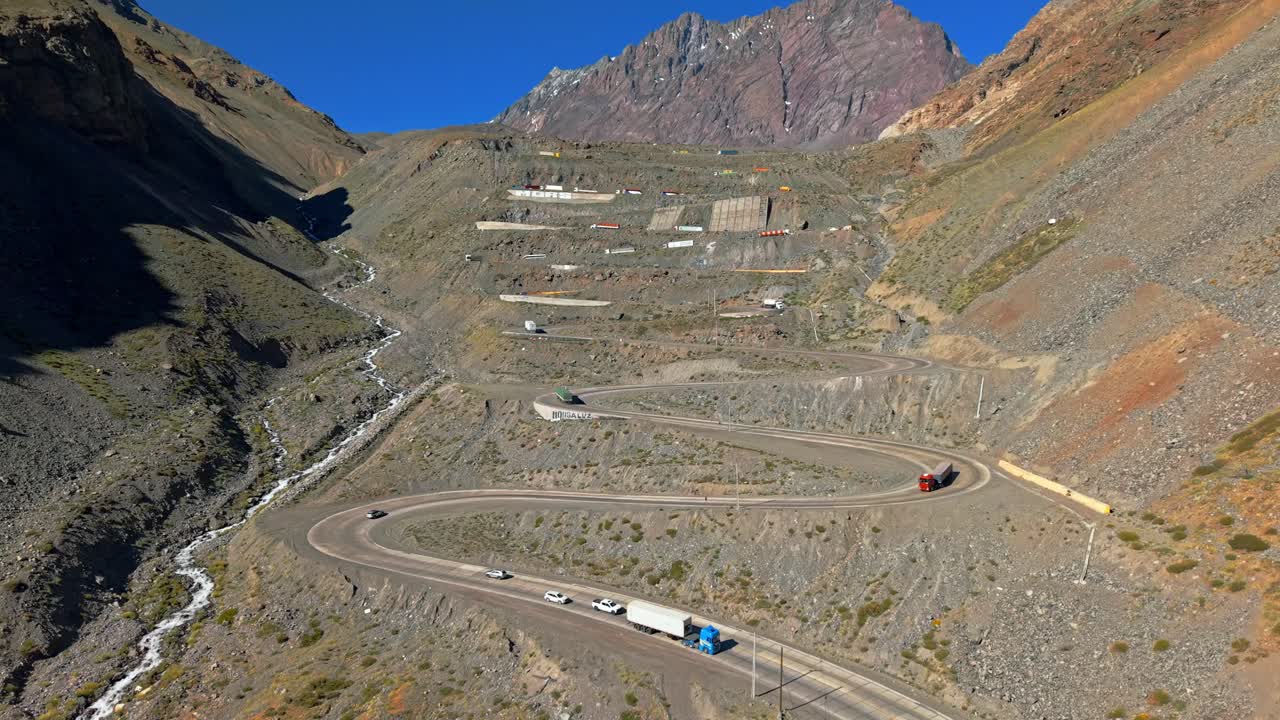 Luftfoto af den panoramiske Cuesta Caracoles på en solskinsdag i Portillo, Chile, med lastbiler, der kører op og ned, og bjergrige omgivelser