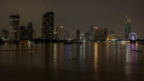 calm dark night scenery at bangkok chao phraya river with boats, skyscrapers and skyline