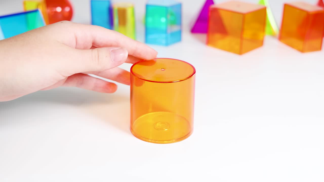 Hands manipulate vibrant 3D geometric shapes on a white surface, highlighting educational and playful exploration in a bright setting
