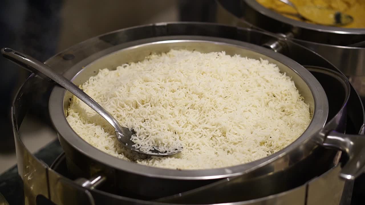 primer plano de arroz cocido caliente con vapor servido en un recipiente de acero en buffet