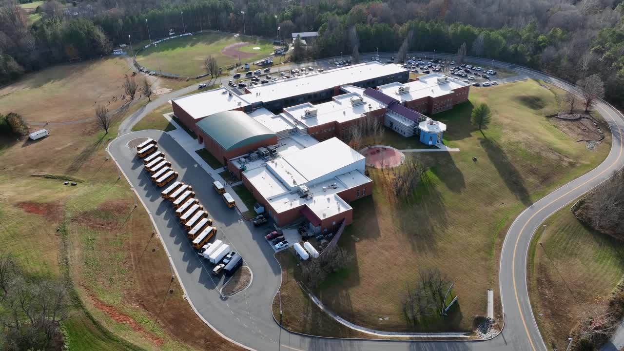 Last yellow school bus arriving school building in rural scenic suburb district row American town. Sunny day in fall season. Aerial top down shot