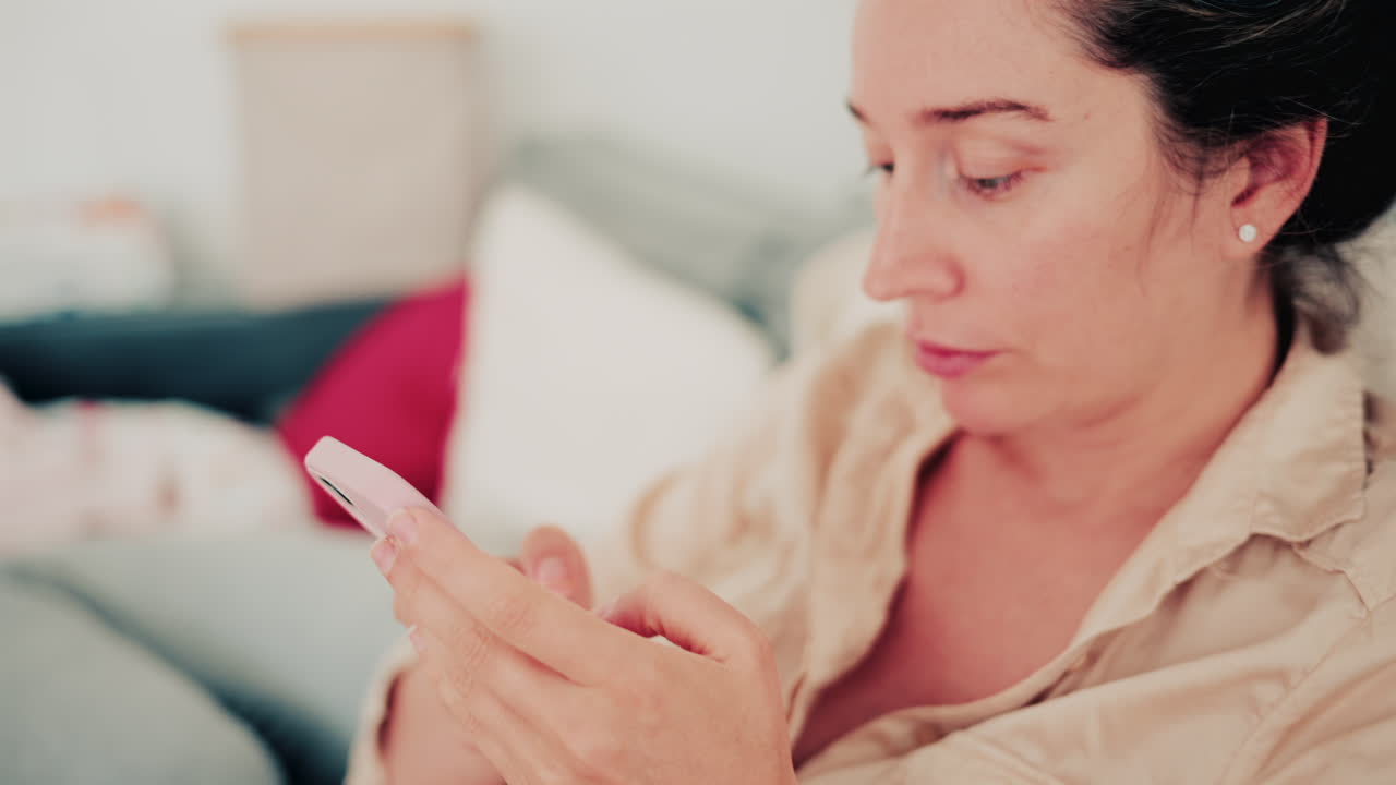 A woman sits on a sofa in soft natural light, focused on her smartphone