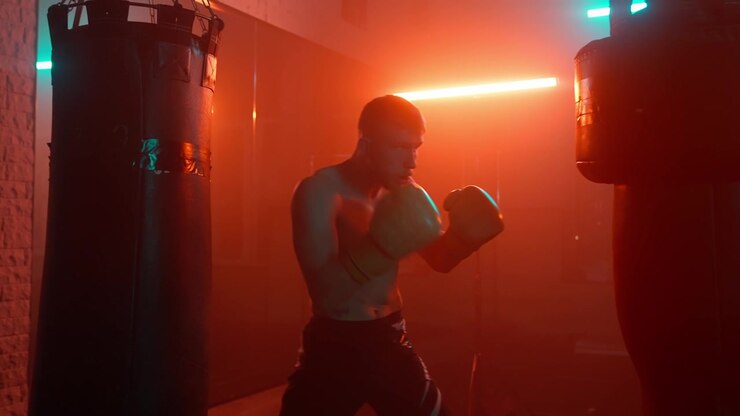 Pugile che si allena con un sacco da boxe in una palestra buia illuminata al neon.