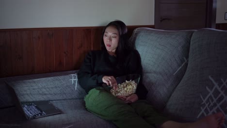 Young-Asian-woman-sitting-on-sofa-and-eating-popcorn