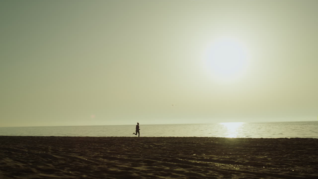 해변에서 달리는 알려지지 않은 스포츠 선수. 해가 지는 동안 조 ⁇ 하는 여성의 실루 ⁇ .