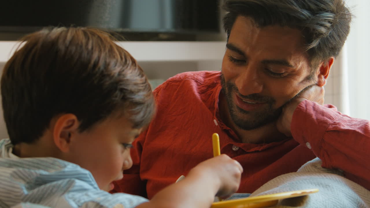 padre e hijo en casa en el sofá en la sala de estar jugando con el juego de dibujo juntos