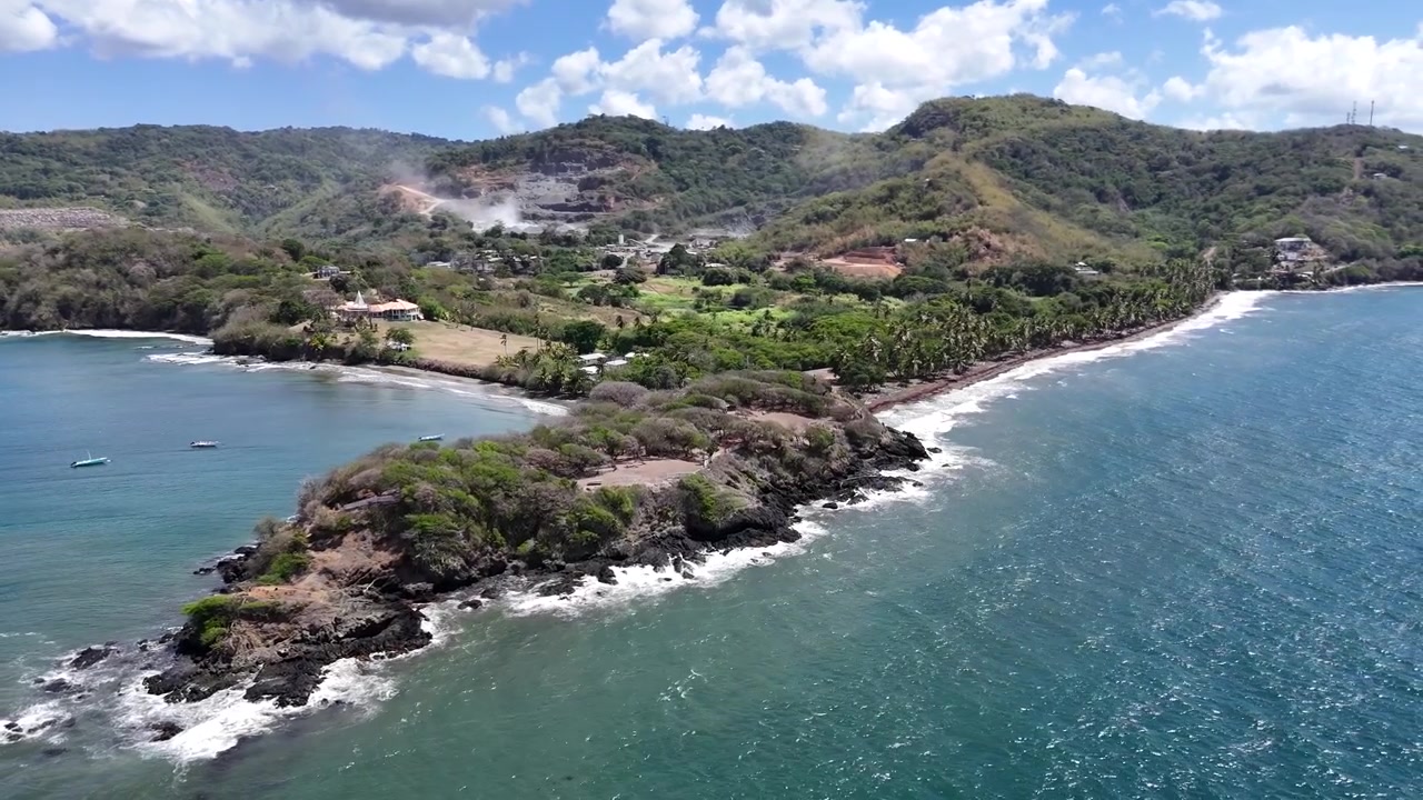 Volo panoramico con drone lungo la costa fiancheggiata da palme di Granby Fort. Onde caraibiche spumeggianti che si infrangono sulla spiaggia vulcanica tropicale dell'isola di Tobago, Trinidad e Tobago
