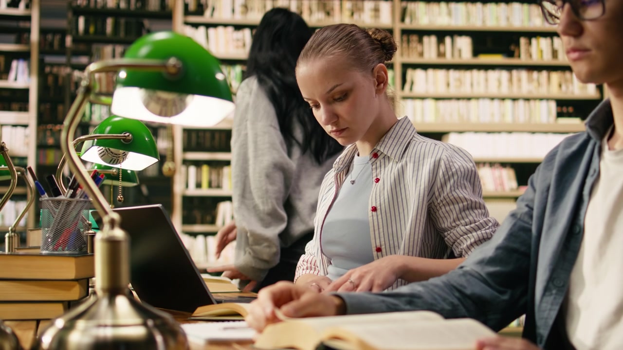 Giovane studente che prende appunti sul laptop per un compito universitario nella biblioteca universitaria.