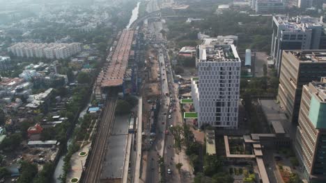 Aerial-Shot-of-Metro-In-Chennai-City-With-IT-Buildings,-Bridge,-Highway-Filled-With-Cars-And-Traffic