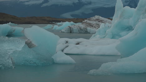 Glaciers-floating-in-Glacier-Lagoon,-Iceland,-with-seagulls-flying-overhead,-against-the-backdrop-of-blue-waters-moving-towards-Diamond-Beach