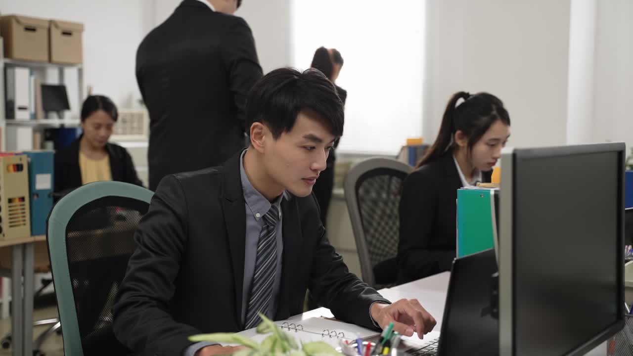 身穿西裝的專注亞洲商務男士，在公司明亮的辦公室內與同事團隊合作，使用手提電腦工作
