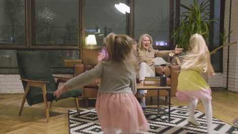 Two-Little-Girls-Running-And-Hugging-Their-Happy-Grandmothers-Who-Sitting-On-Sofa-In-The-Living-Room-At-Home