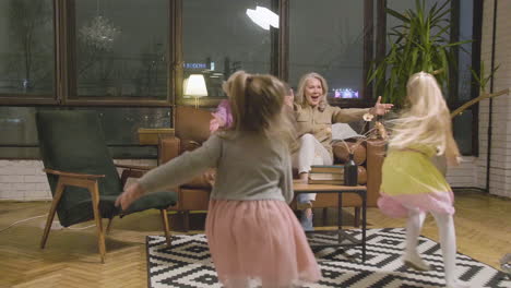 two little girls running and hugging their happy grandmothers who sitting on sofa in the living room at home