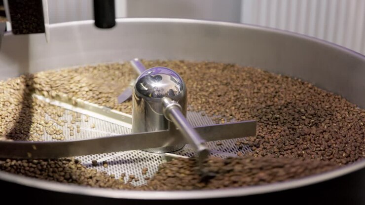 Silver drum machine spins and spreads tumbling coffee beans to roast evenly