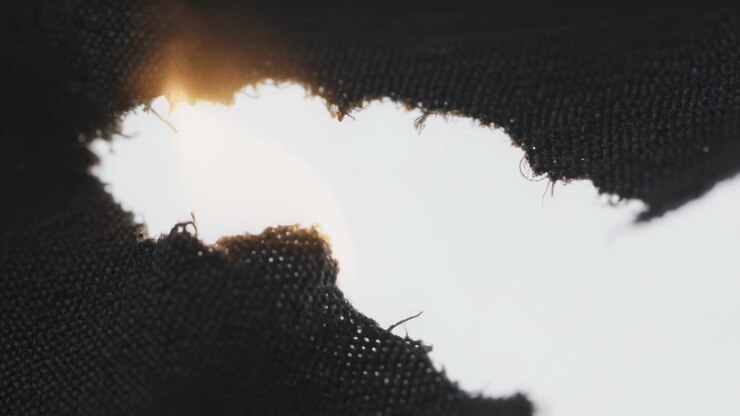 Burning black woven textile growing flame from small orange glow at studio macro, with backlight