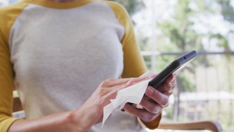 Mujer-Con-Mascarilla-Limpiando-Su-Teléfono-Inteligente-Con-Un-Pañuelo