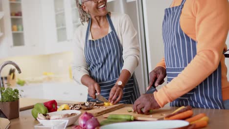 Fröhliches-Afroamerikanisches-Seniorenpaar-In-Schürzen,-Das-Essen-In-Der-Küche-Zubereitet,-Zeitlupe