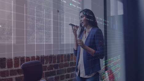 animation of graphs, trading boards, biracial woman talking on speaker of smartphone in office