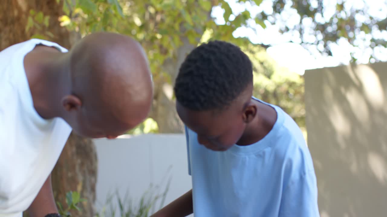 Male mentor and teenage boy lifting solar panel in yard, inspecting cells and discussing setup