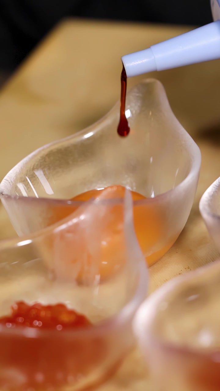 Primo piano di salsa di soia scura che si versa in ciotole di vetro contenenti tuorli d'uovo freschi e crudi.