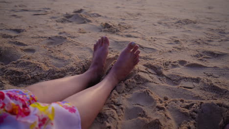 4k video of legs stretched out and resting on the warm, soft sand