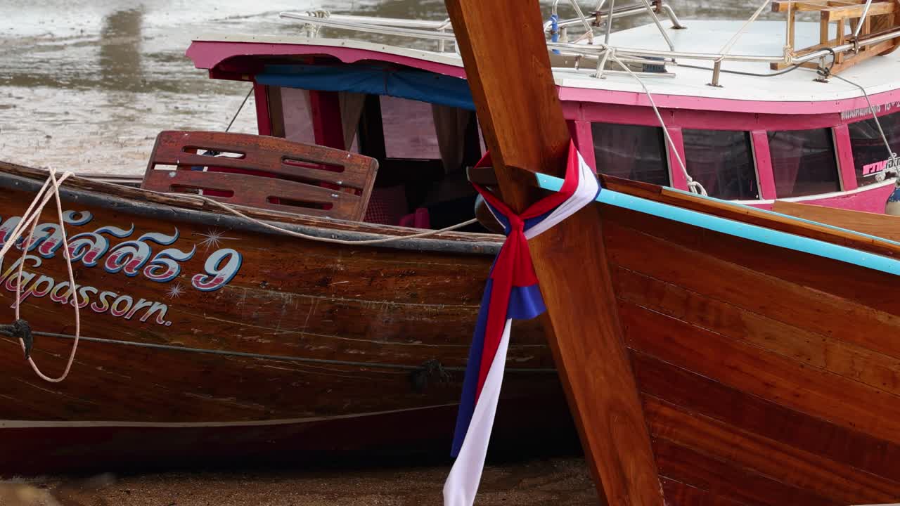 Detailed view of a wooden boat's hull with colorful ribbons and painted details at a dock.