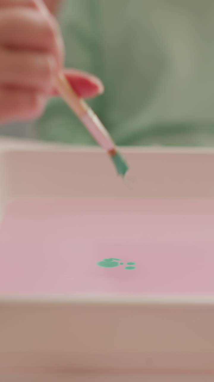 Teacher drips green paint into water showing little student Ebru drawing technique in studio closeup slow motion. Conducting art lesson for child