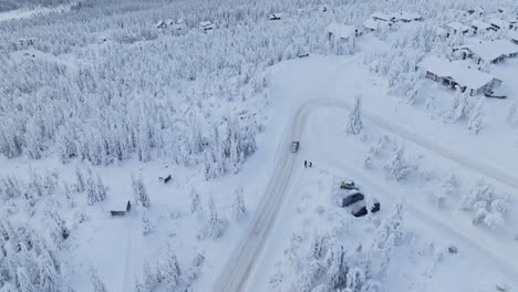 drone tracking a ev car in middle of snowy forest and mountain cabins in lapland