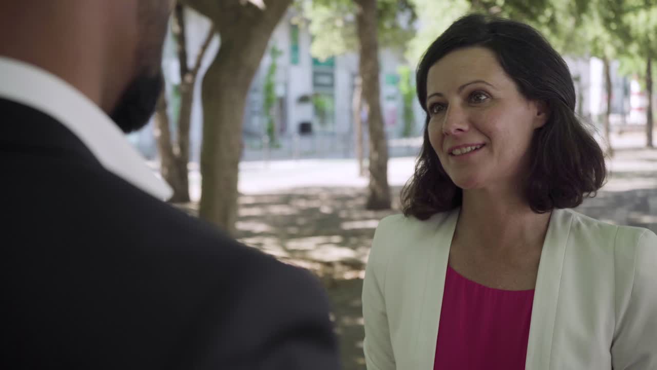 una mujer de mediana edad sonriente hablando con un hombre de negocios al aire libre.