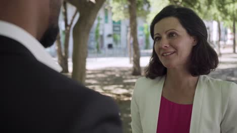 smiling middle aged woman talking with businessman outdoor.