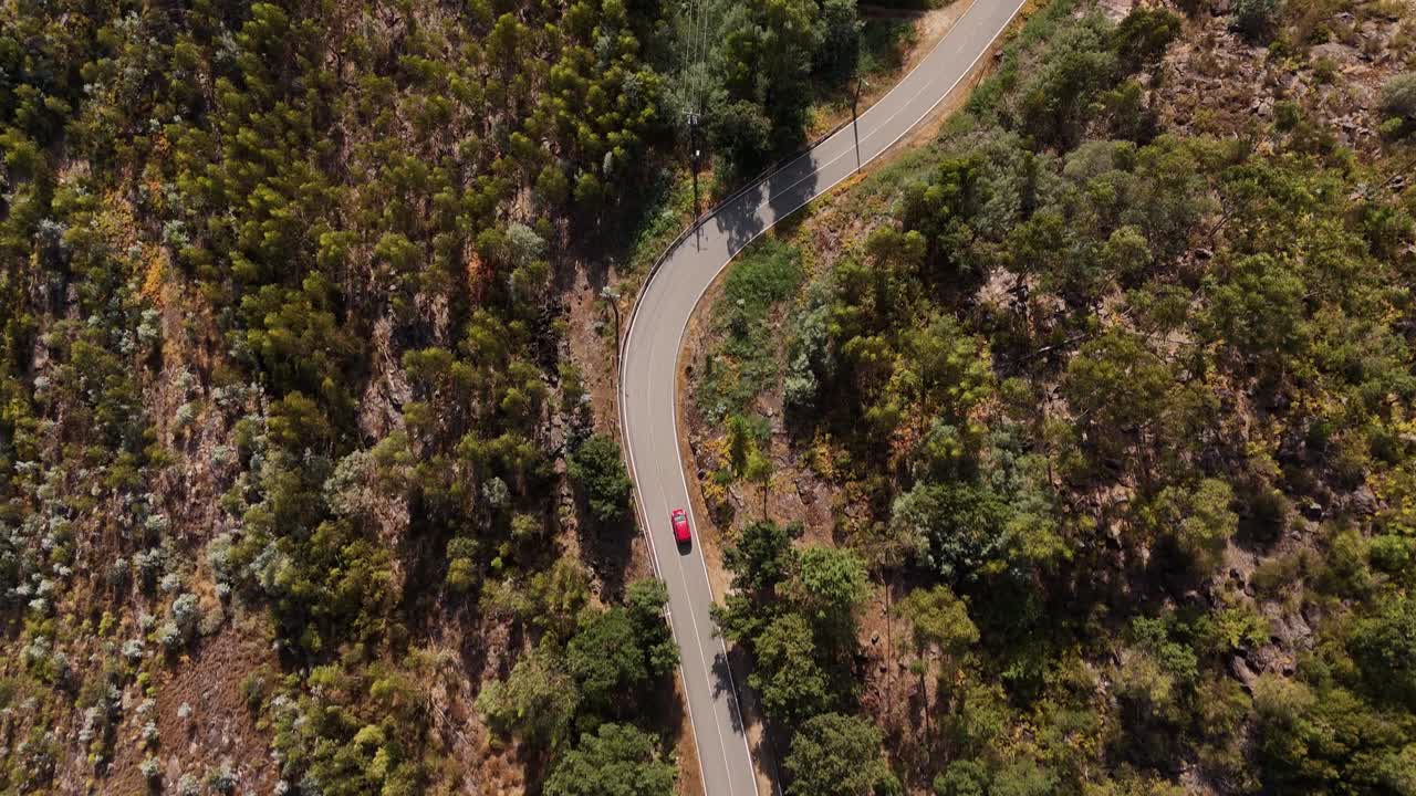 red car traveling along a winding road through rugged terrain in Minho, North Portugal - aerial