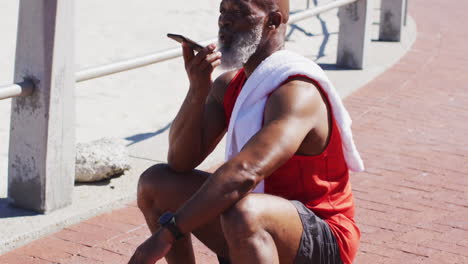 senior african american man talking on the smartphone while sitting on basketball on the court near