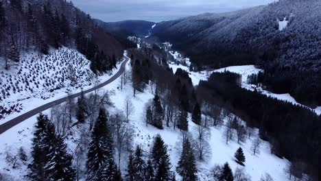 Vista-Aérea-En-Vuelo-Bajo-De-Una-Carretera-De-Montaña-Con-Bosques-Nevados-Durante-El-Invierno-En-Altos-Vosgos,-Francia