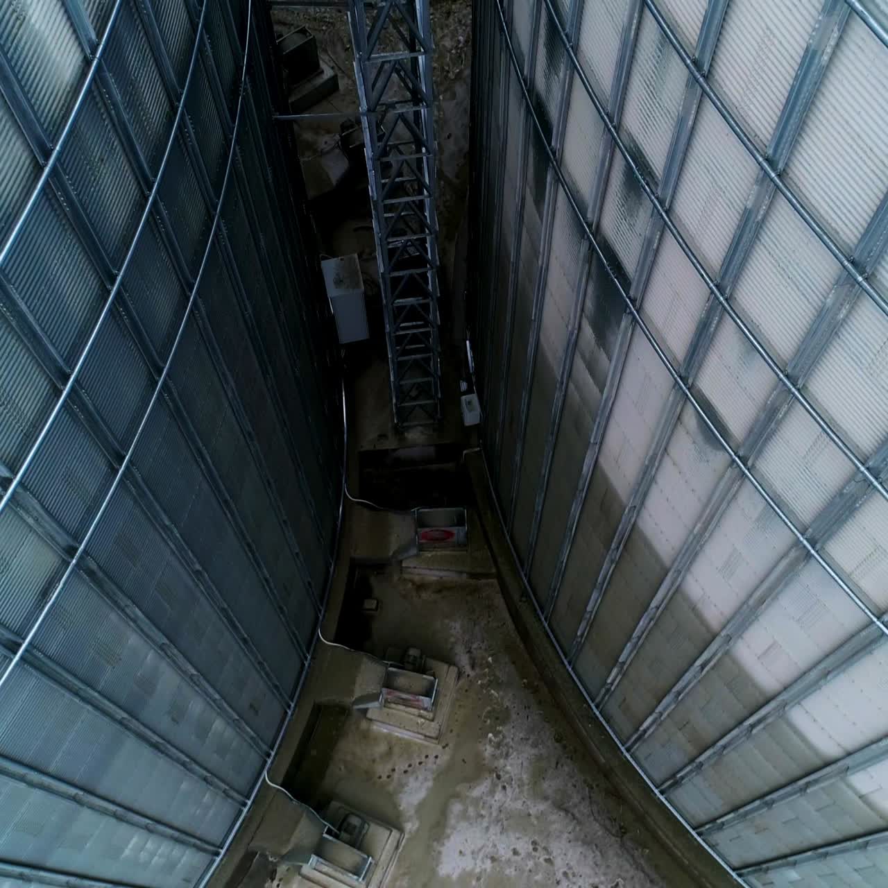 Going down among two huge metal granary tanks. Exterior footage of the modern silo complex on winter day
