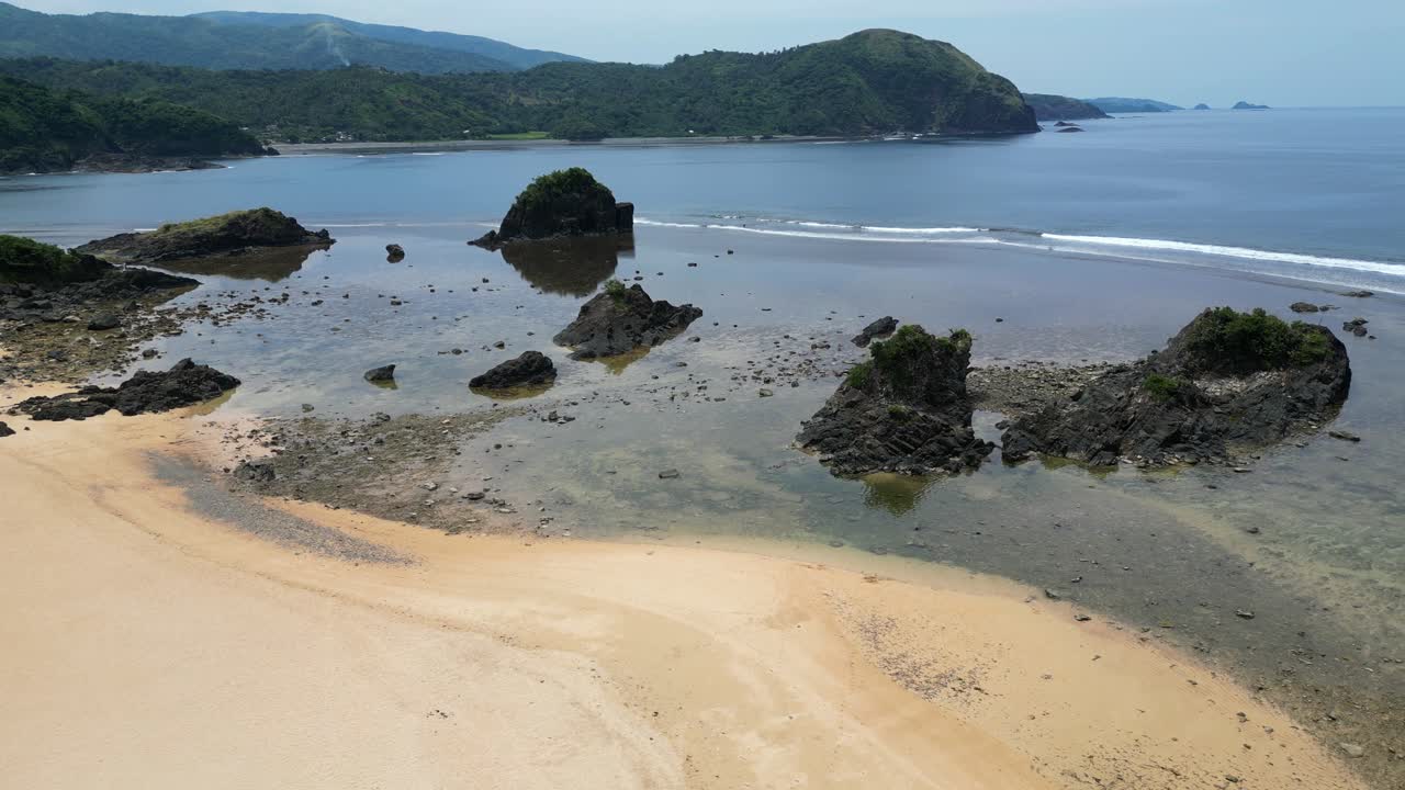 Rekaman dolly udara garis pantai saat air surut di resor pantai pasir putih dengan bebatuan besar dan terumbu karang di Baras, Catanduanes