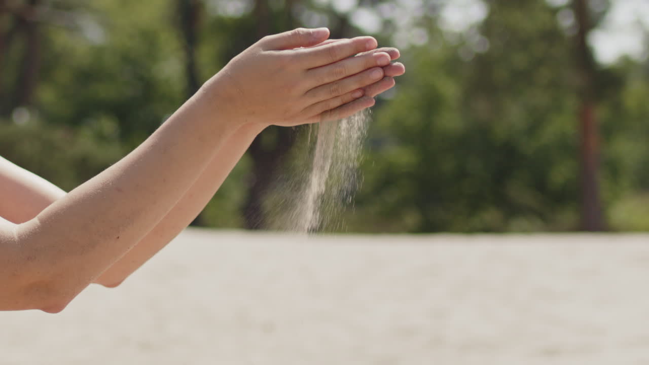 Close up of sand seeping through the fingers of a woman on a beach on a sunny, summer day