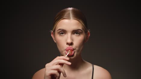 naughty caucasian woman licks tasty lollipop, isolated black background