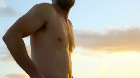 vista lateral de un hombre caucásico adulto con traje de surf en la playa durante la puesta de sol 4k