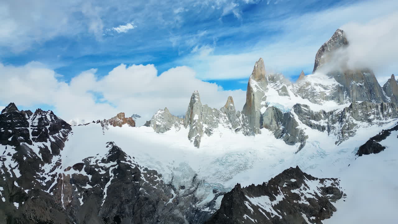 Aerial drone view of two deep blue glacial lakes separated by rocky ridges and surrounded by snow covered mountains in slow motion