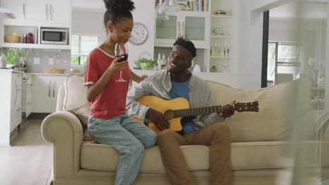 video of happy african american couple sitting on sofa, singing and playing guitar