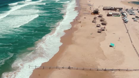 A-lonely-surfer-walks-on-the-beach-while-the-wild-endless-sea-crushing-waves-on-the-sand's-coast-line