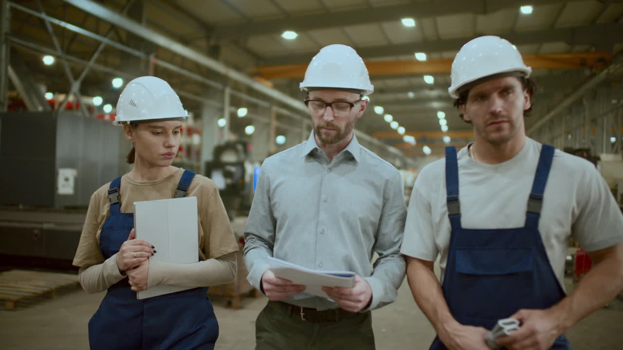 инженер и техники прогуливаются по промышленному заводу, обсуждая машины