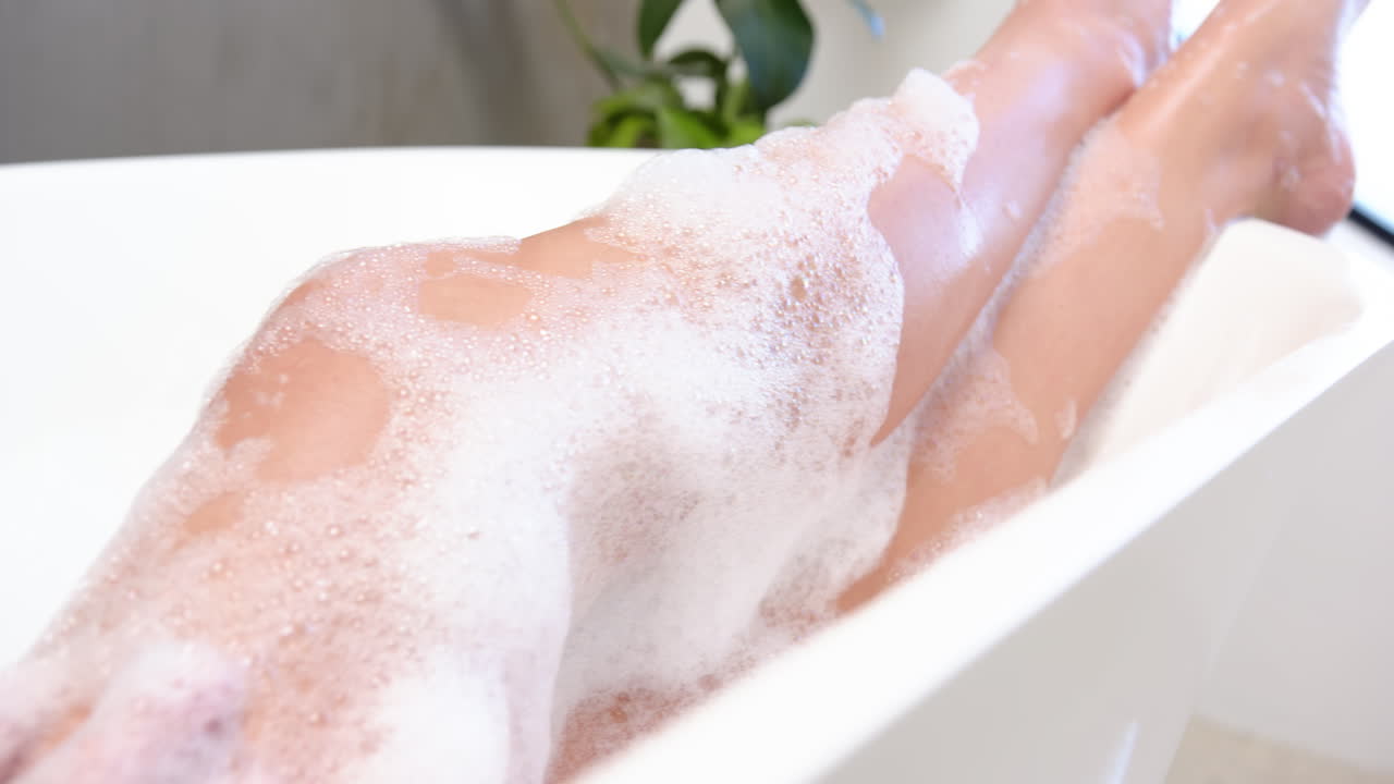 Relaxing in bathtub, woman enjoying bubble bath with plant in background