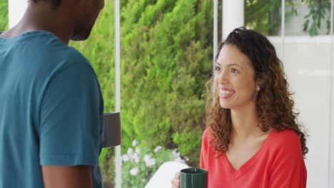feliz mujer biracial bebiendo café con un compañero masculino en el patio