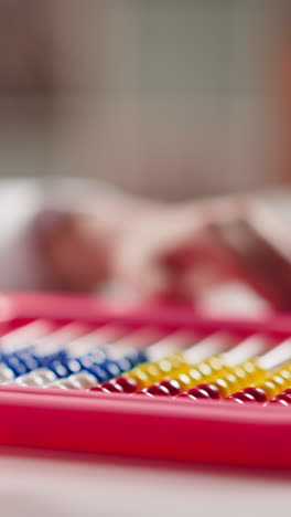 little pupil holds colorful toy abacus and adjusts small beads to learn traditional calculations at table in classroom extreme closeup slow motion